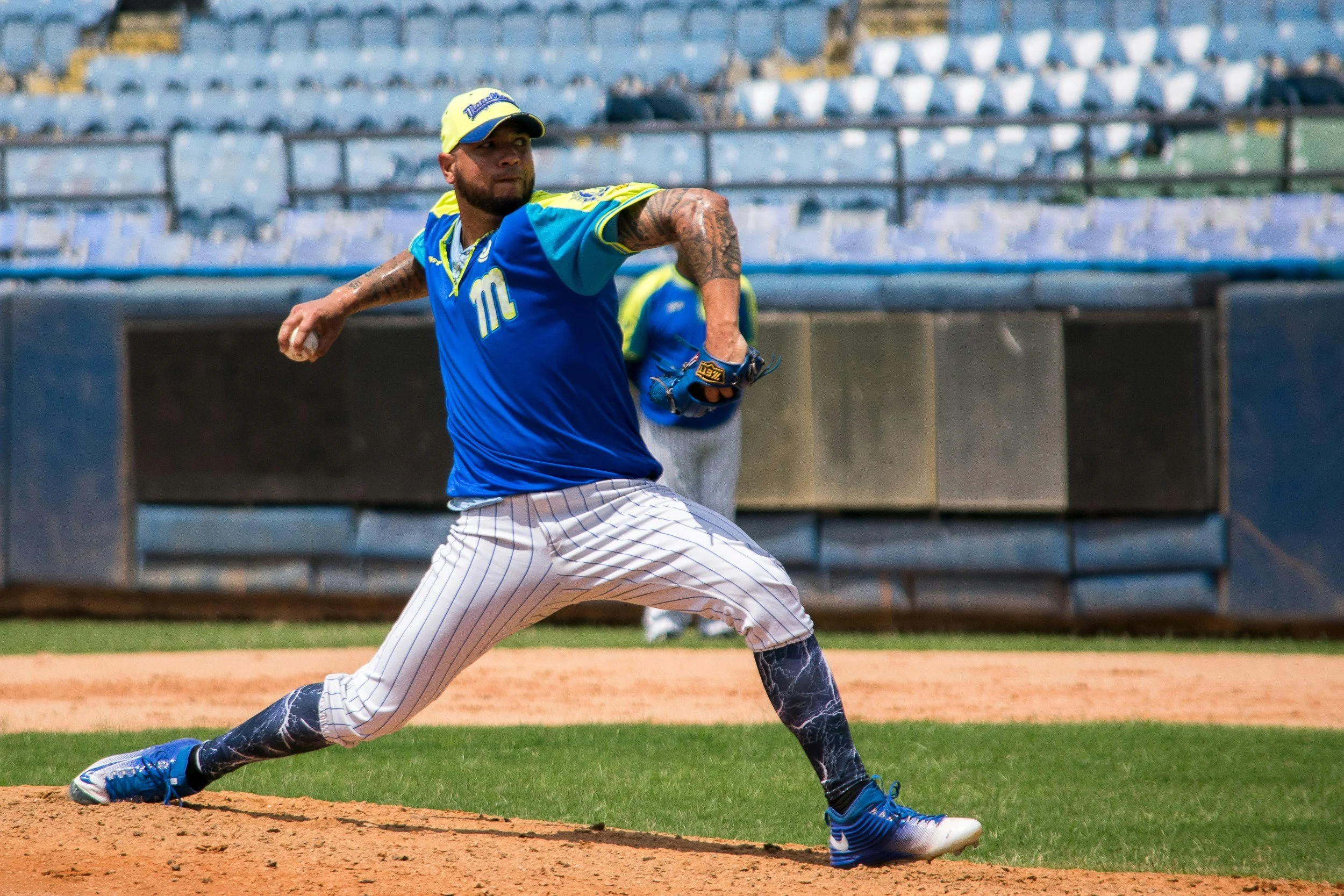 A baseball player in a blue uniform with yellow accents, throwing a pitch on the baseball field.