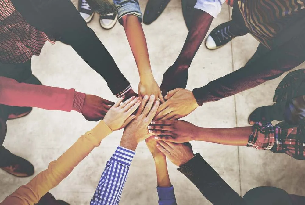 Multiple people placing their hands together in the center, showing unity and teamwork.