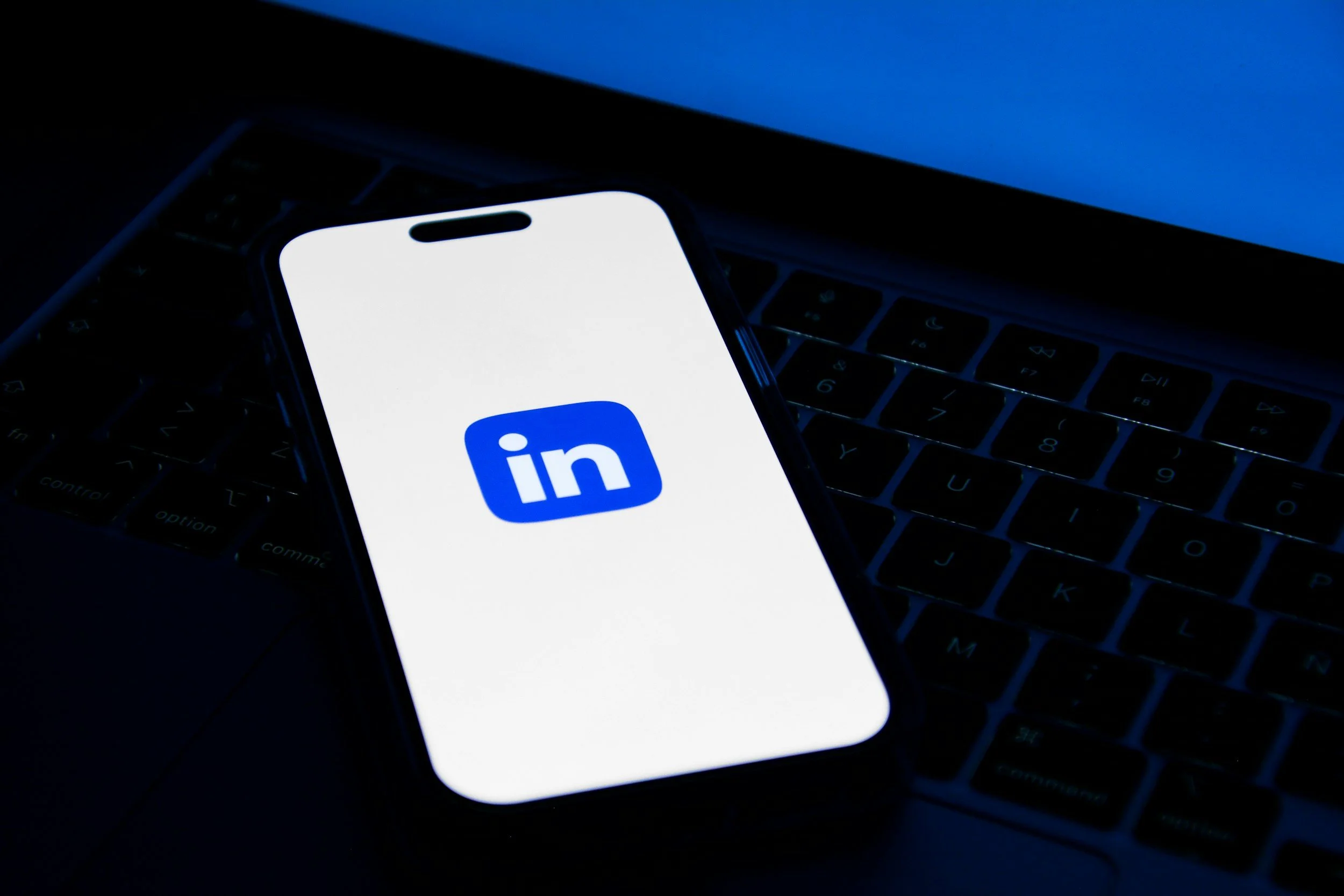 Smartphone with LinkedIn logo on the screen resting on a laptop keyboard.