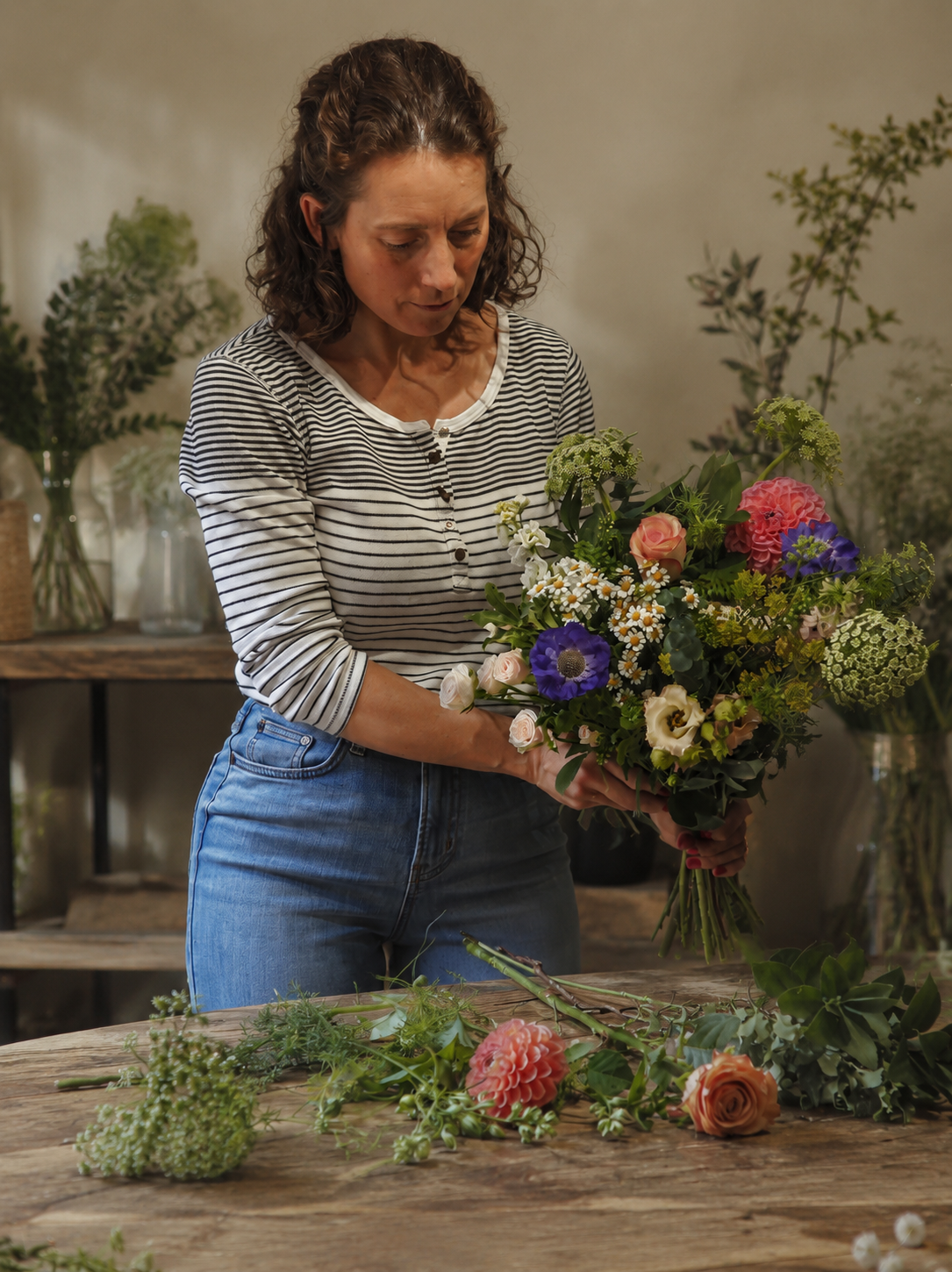 A woman arranging a large colorful bouquet of flowers in a flower shop.