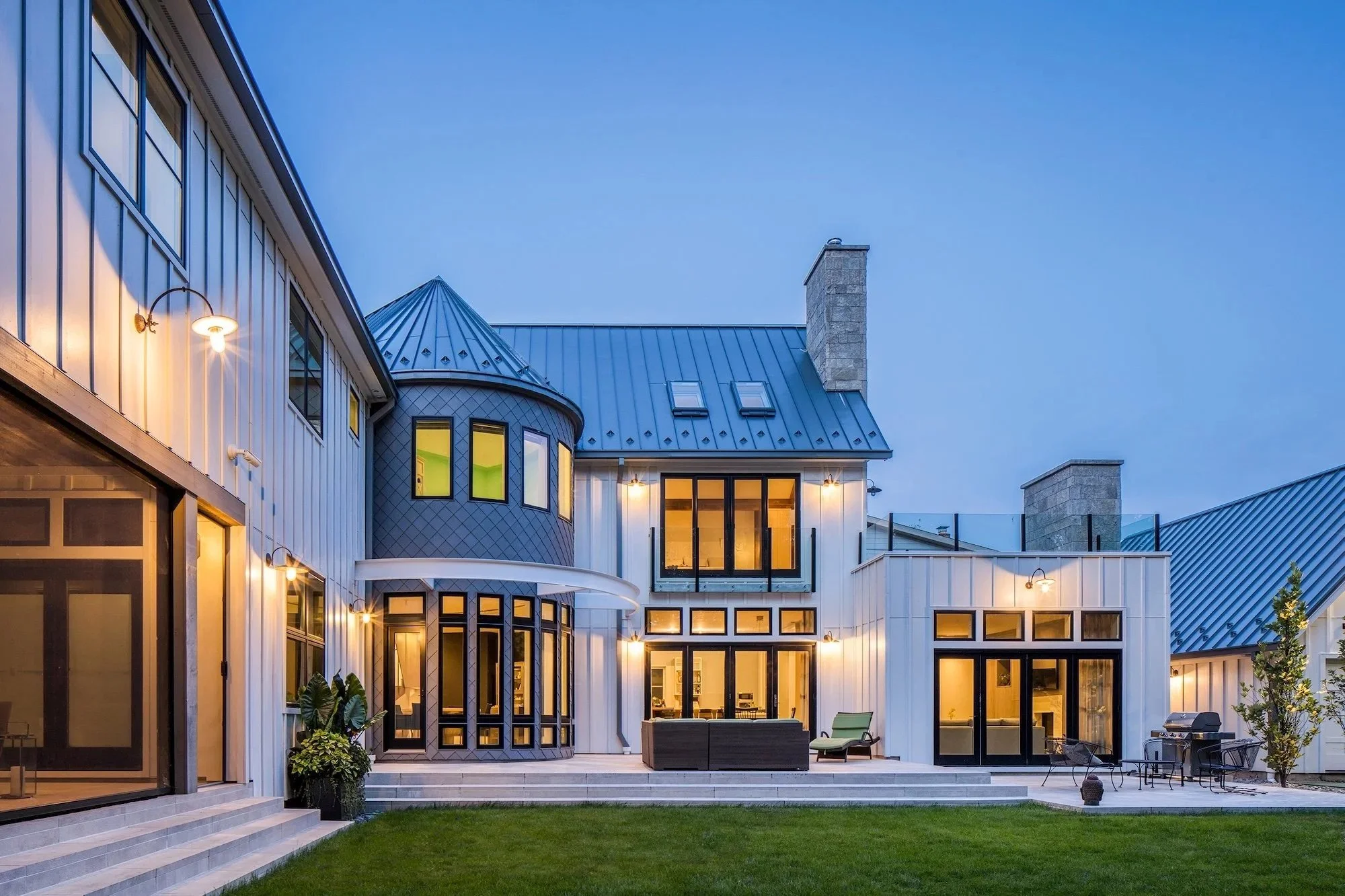 The exterior of a modern farmhouse home featuring large windows and warm interior light.
