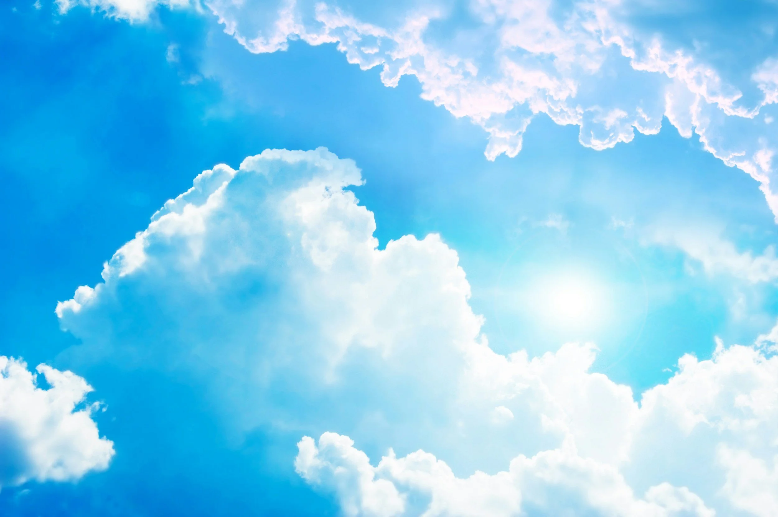 Sun shining through blue sky with white clouds.