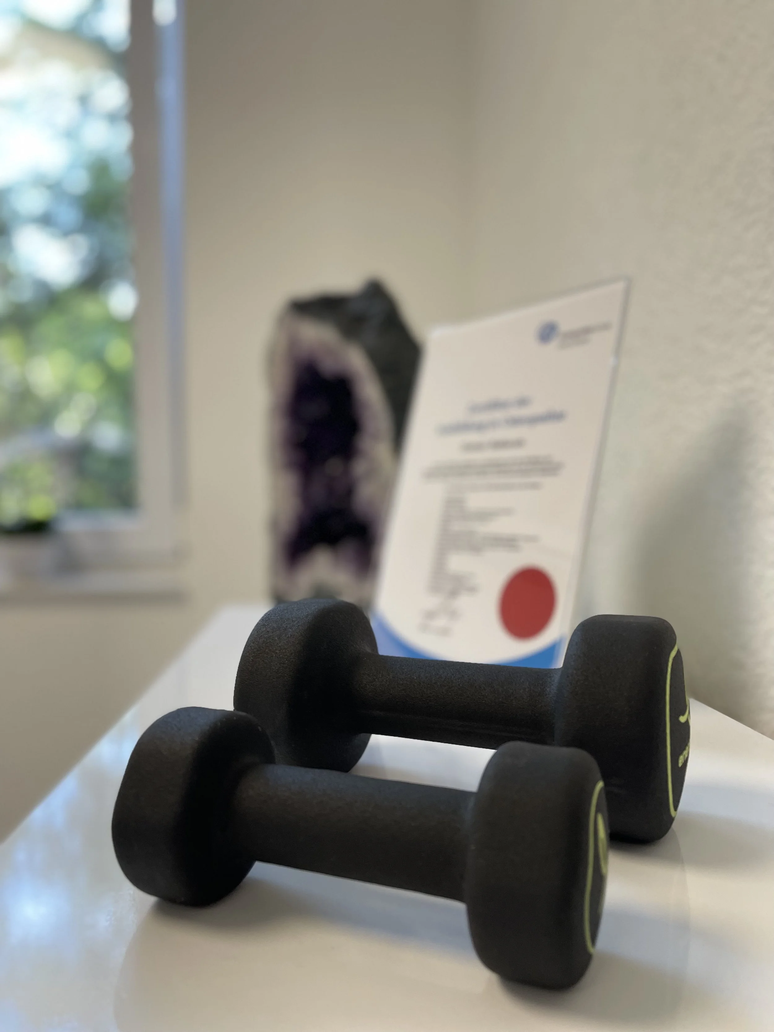 Ein schwarzer Fitnessball liegt auf einem Schreibtisch, im Hintergrund sind Fenster und eine Wand sichtbar.