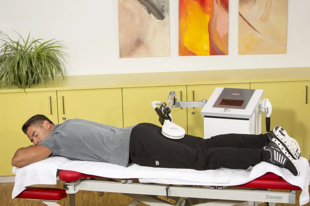 Ein Mann liegt auf einer bequemen Liege in einer medizinischen Einrichtung, während ein medizinisches Gerät an seinem Rücken angebracht ist, vermutlich eine Innovation in der Physiotherapie oder Schmerzbehandlung.