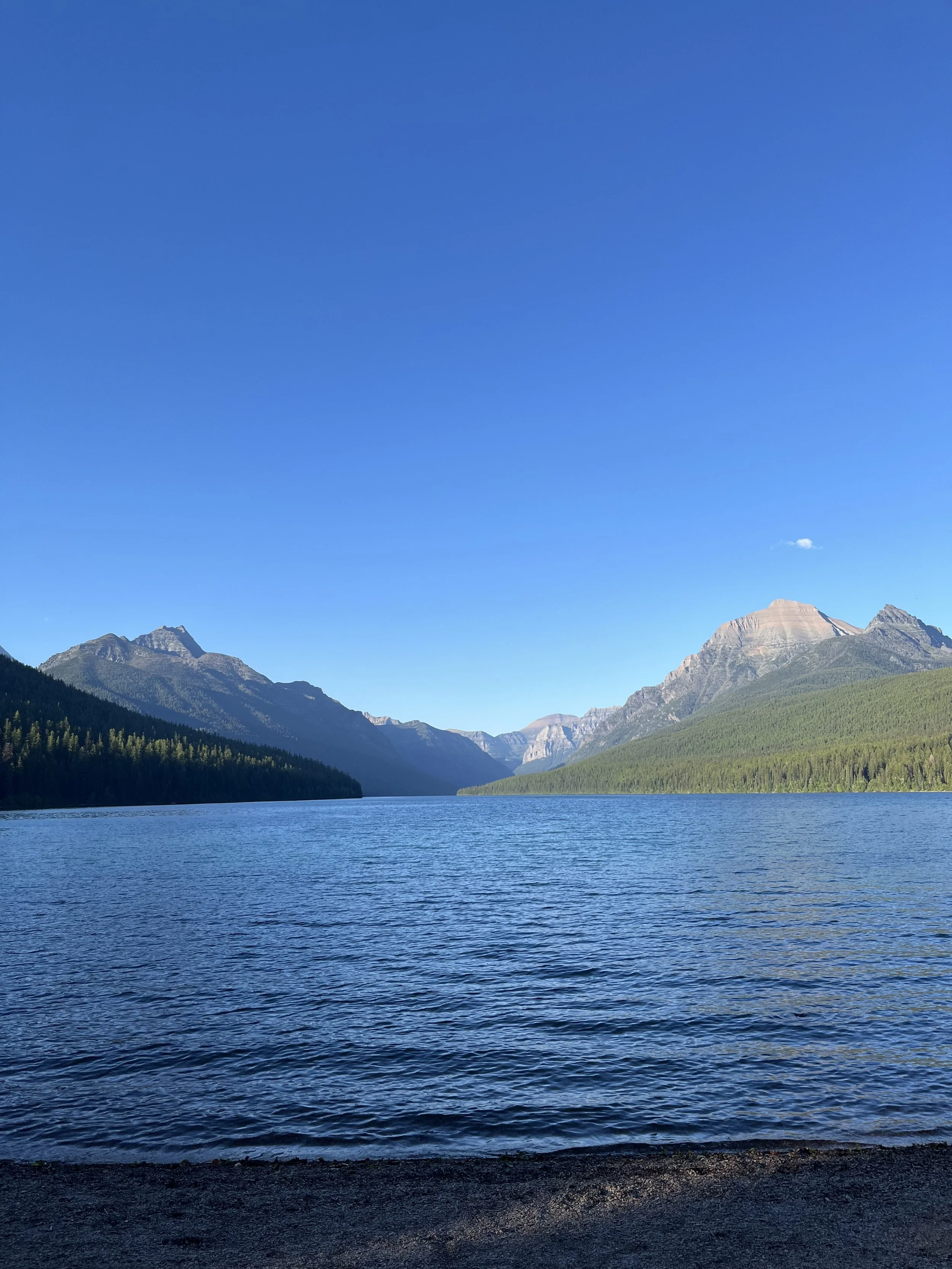 A peaceful lake surrounded by mountains under a clear blue sky.