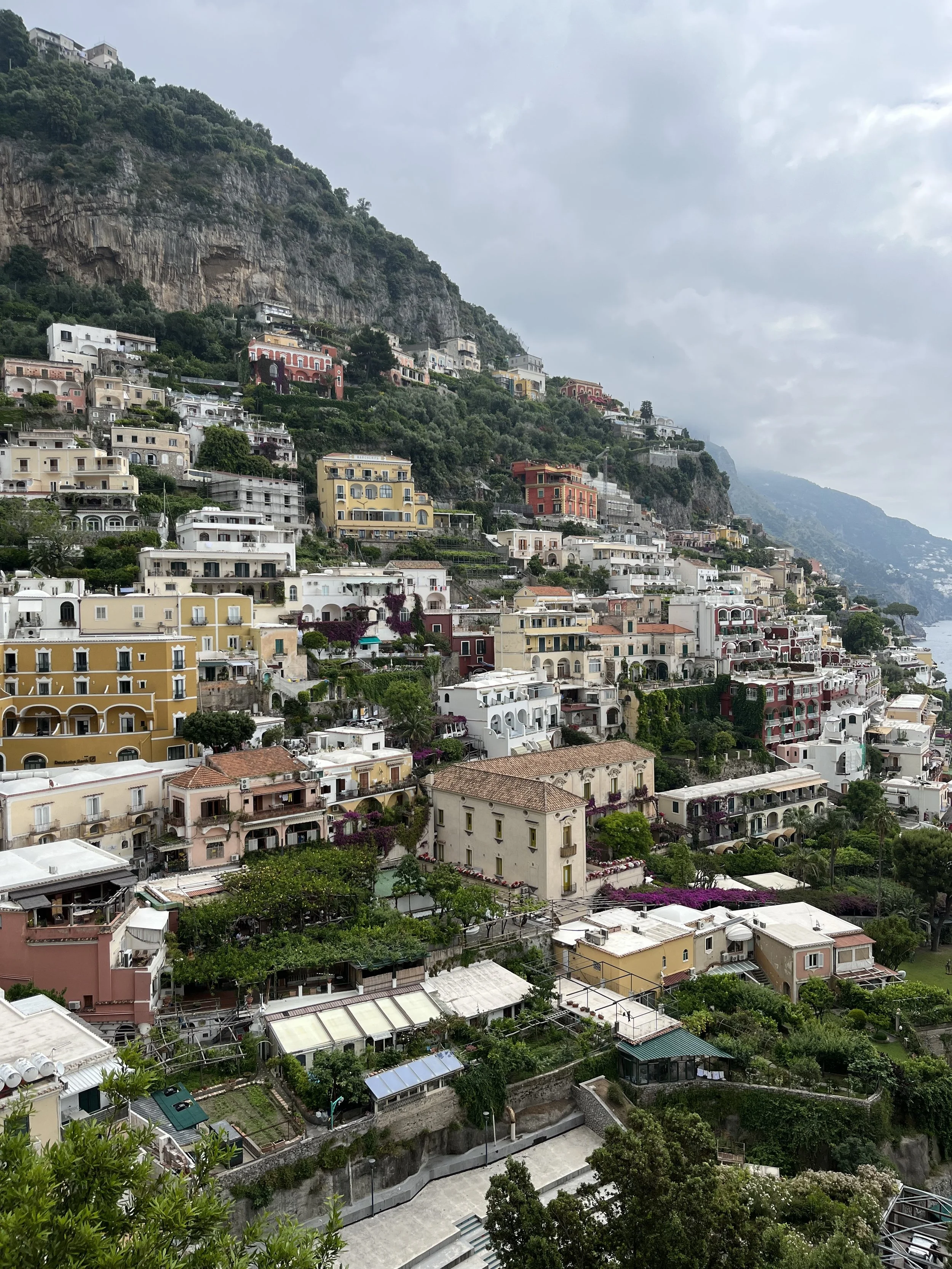 Houses and buildings built along a hillside on the Amalfi Coast in Italy, with lush greenery and a cloudy sky.