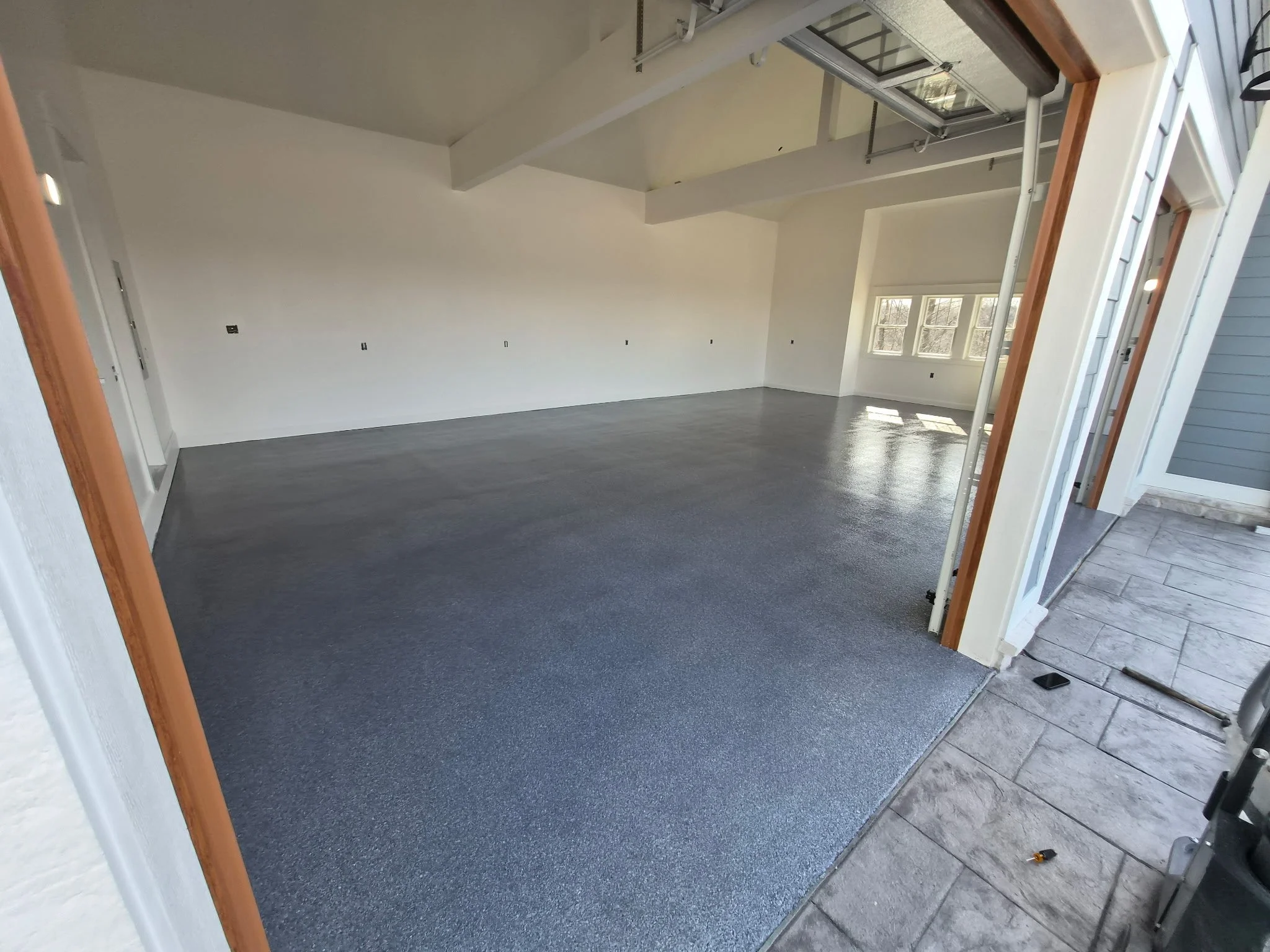 Empty room with white walls, large windows, a gray carpeted floor, and some construction materials and tools near the entrance.