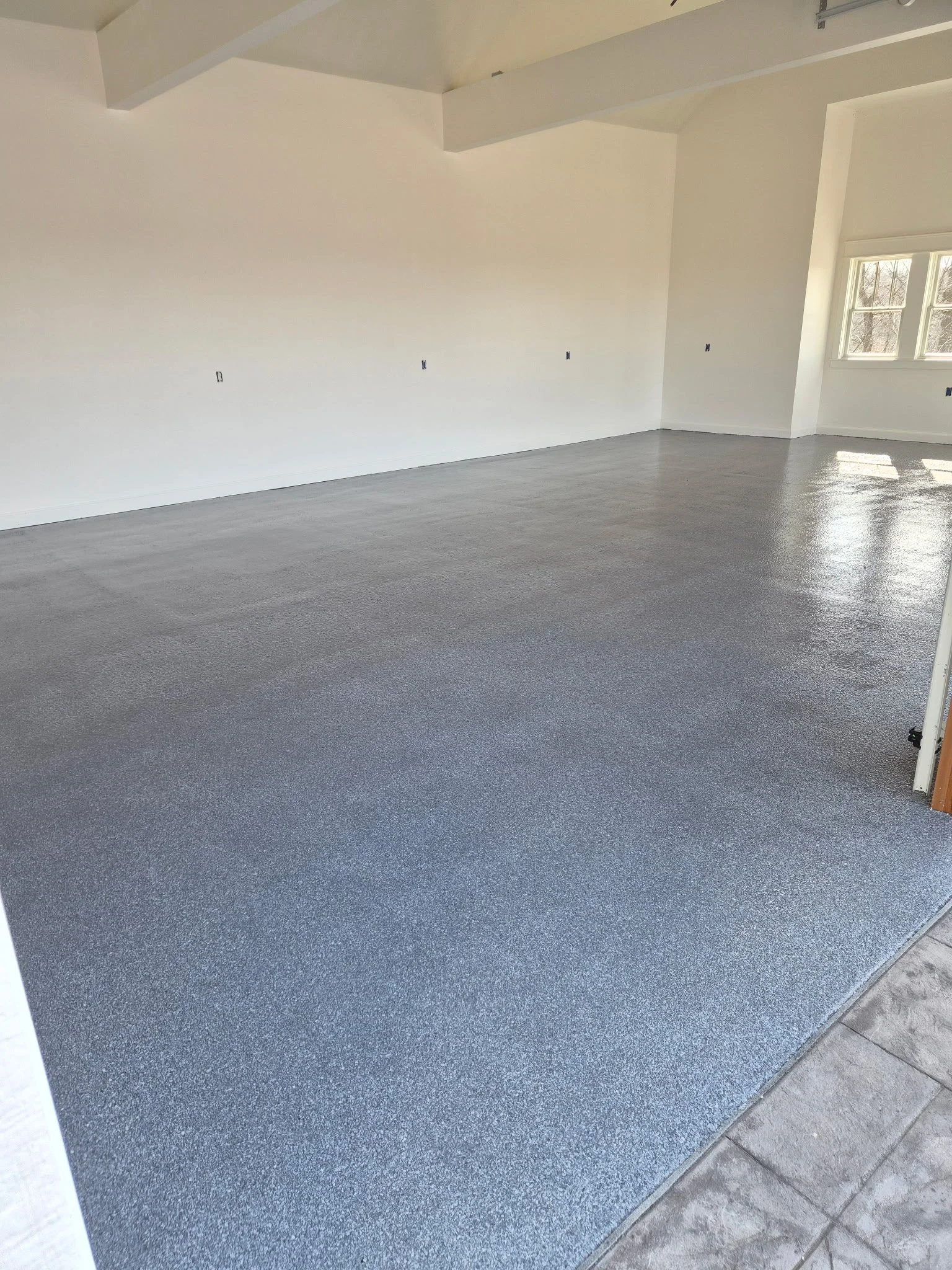 Empty room with new gray epoxy flooring, white walls, and a large window.