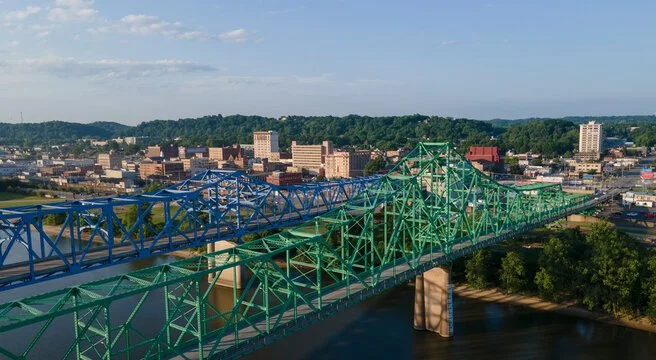 Aerial view of Ashland, KY with the twin bridges spanning the Ohio River, with buildings and hills in the background.