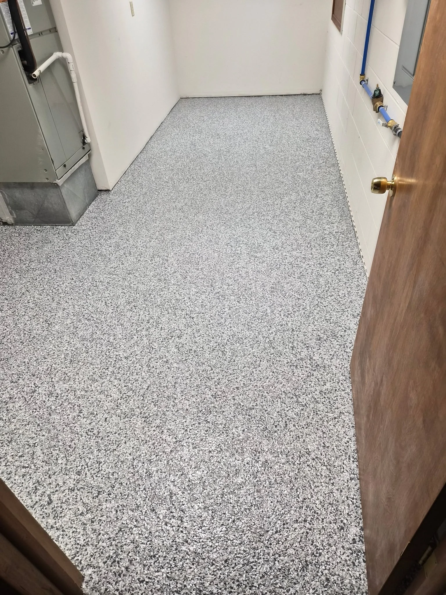 Empty utility room with gray speckled flooring, white walls, utility pipes and electrical panel.