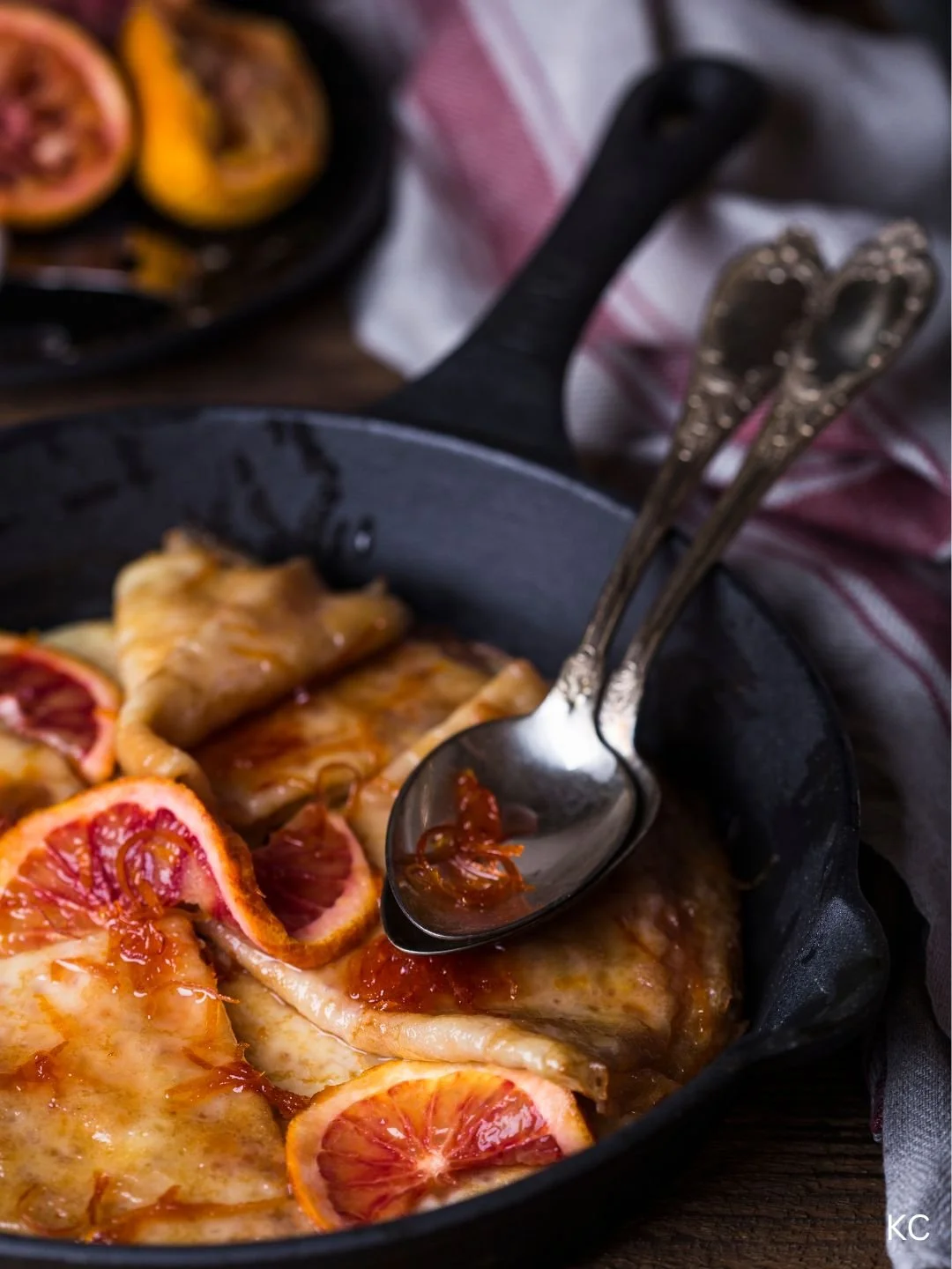 Sliced blood oranges on baked chicken in cast iron skillet with serving spoons