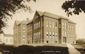 Black and white photo of a large, old brick school building with multiple stories and a symmetrical facade.