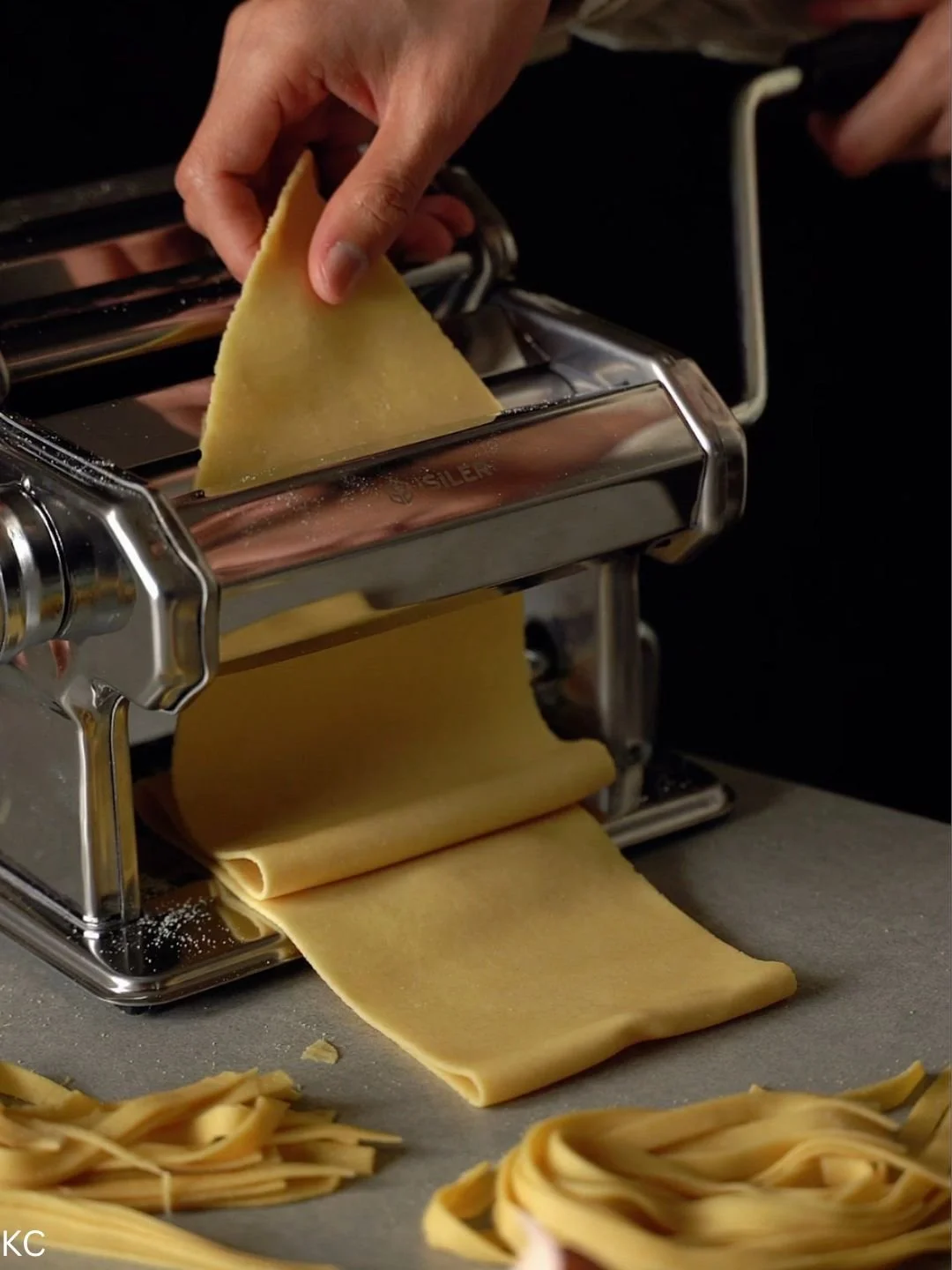 A hand using a pasta machine to roll out fresh pasta dough.