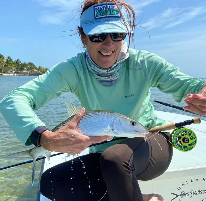 Smiling angler holding a bonefish caught on fly rod in the Florida Keys, ready for release in shallow clear water.