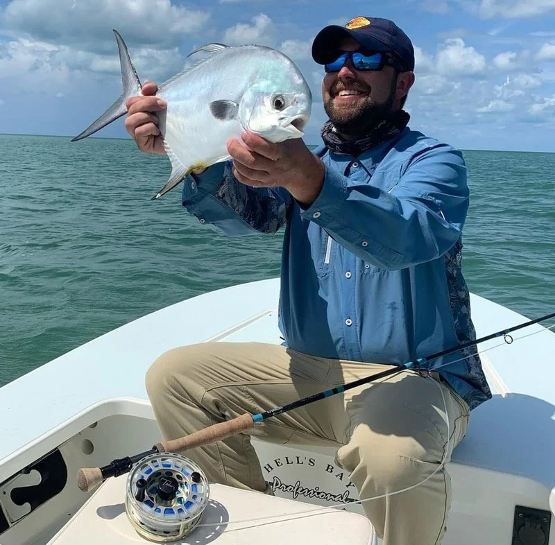 Happy angler holding a permit caught on fly rod in the Florida Keys, sitting on a skiff with turquoise water behind.