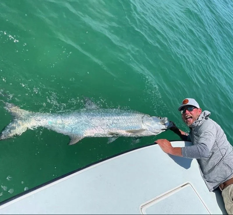 “Angler holding a giant tarpon beside the boat in clear green water during Florida sport fishing trip.”