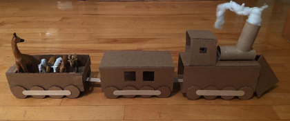 Cardboard train with a horse and two puppies in a wagon attached to a cardboard engine with smoke coming from the chimney.