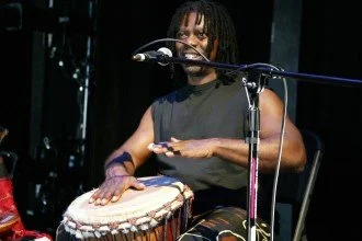 Person playing a drum and singing into a microphone during a performance.