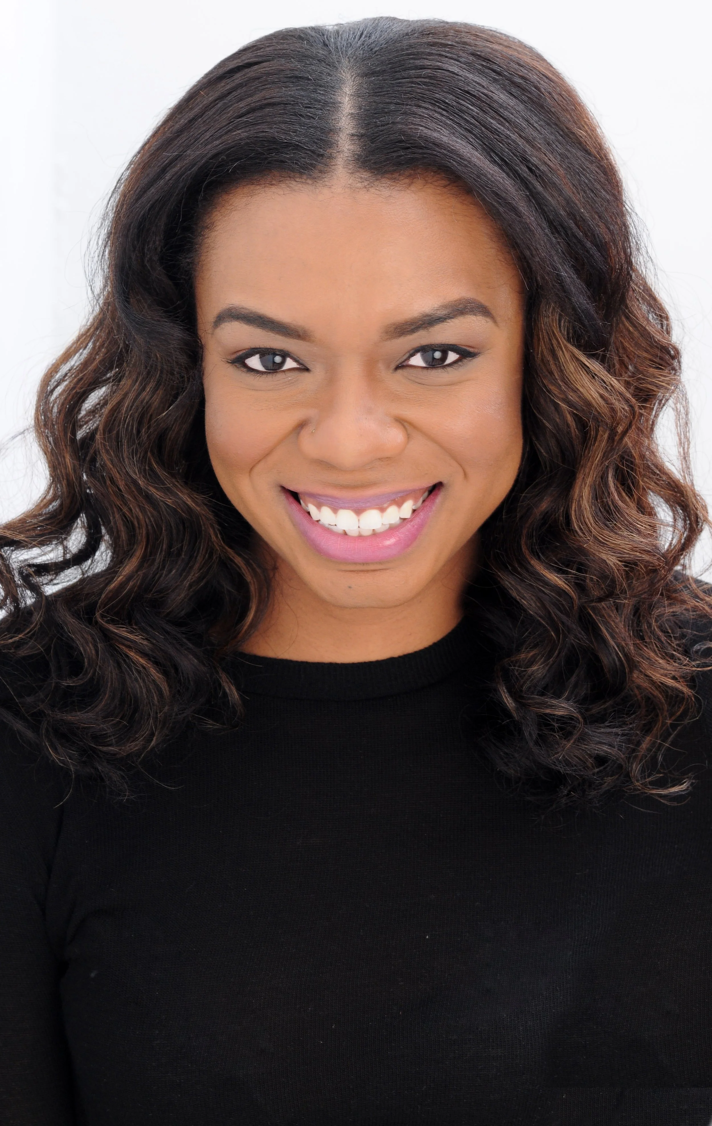 A smiling woman with dark wavy hair, wearing a black top, with a white background.