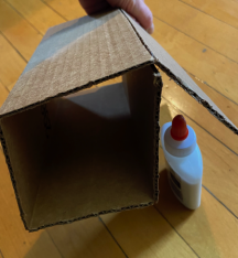 A cardboard box with a glue bottle next to it on a wooden surface.