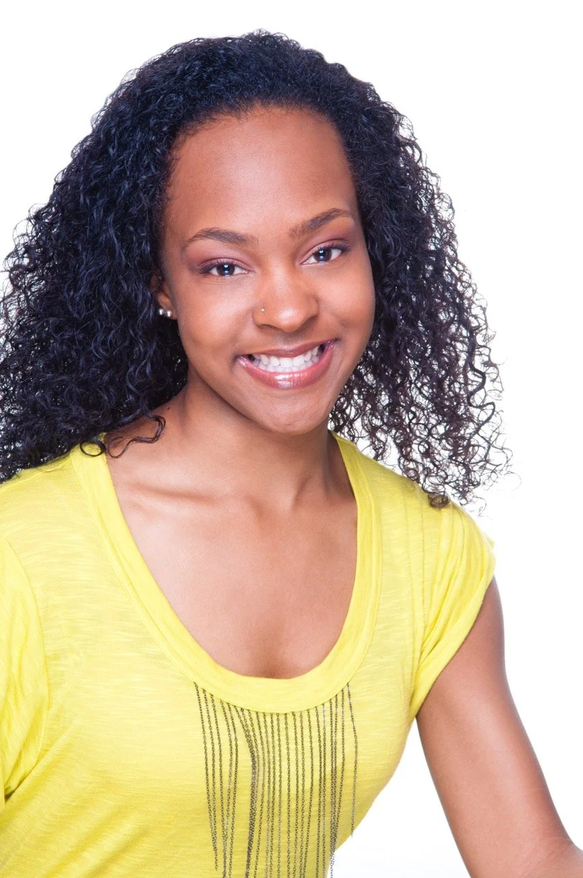 A woman with curly black hair and a yellow top, smiling softly at the camera.