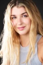 A young woman with long blonde hair, blue eyes, and a light gray top, smiling softly at the camera.