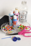 Assorted arts and crafts supplies including bottles of paint, a jar of water, scissors, colored pins, and a pincushion with pins.
