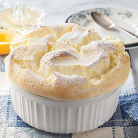 A baked lemon meringue pie with a golden crust and fluffy whipped meringue on top, in a white ceramic dish with a side plate and spoon.