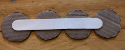 Four round chocolate cookies with a white popsicle stick on top, placed on a wooden surface.