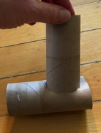 Hand holding a cardboard tube upright on a T-shaped cardboard structure