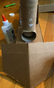 Cardboard box with a paper tube and bottles of glue on a wooden surface.
