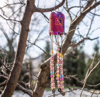 A decorative hanging ornament with beads and a small colorful bag hanging from a tree branch outdoors.