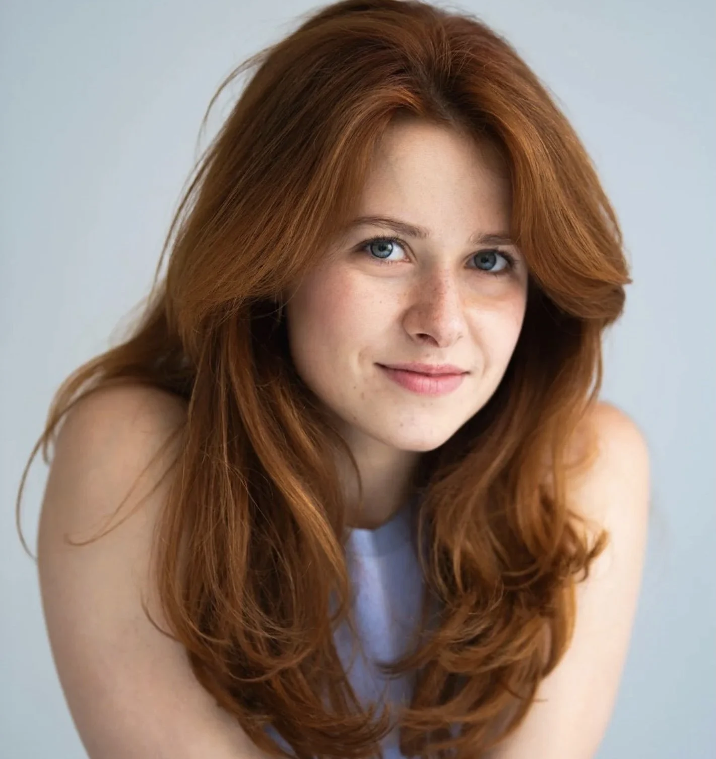 A young woman with red hair smiling, wearing a black top against a neutral background.