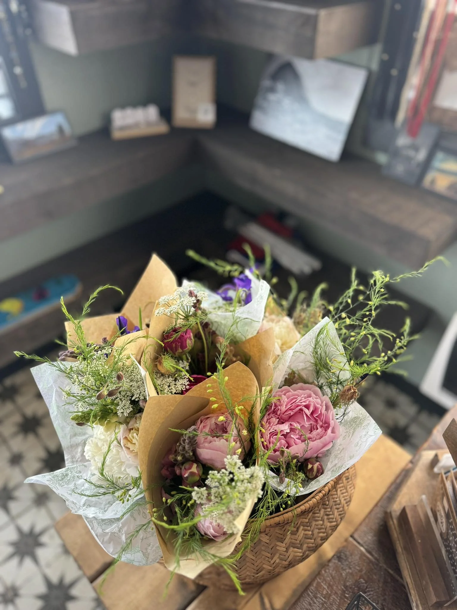 A bouquet of pink, white, and purple flowers arranged in a woven basket on a wooden table.