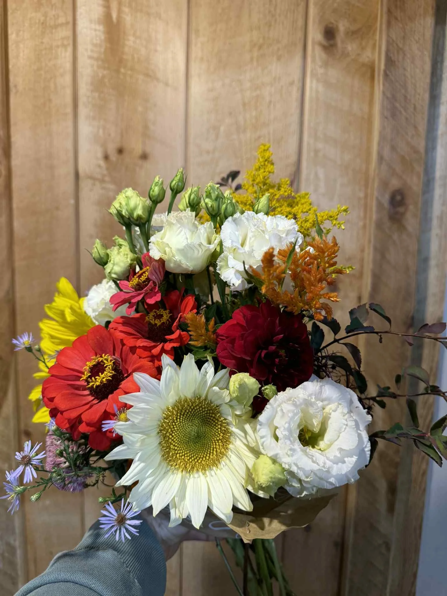 A hand holding a colorful bouquet of flowers against a wooden background.