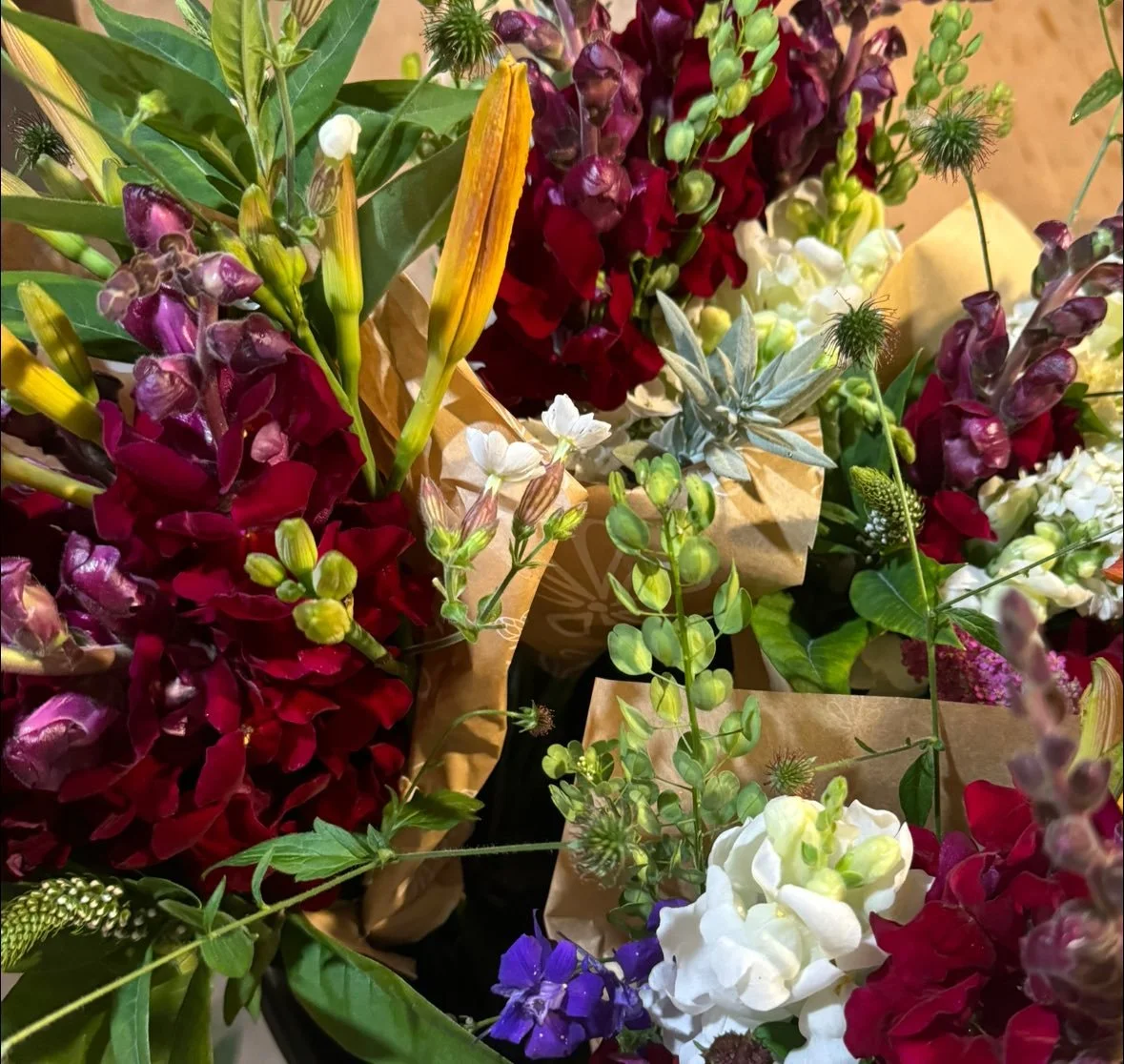 A close-up of colorful flower bouquets with red, purple, white, and green flowers wrapped in brown paper.