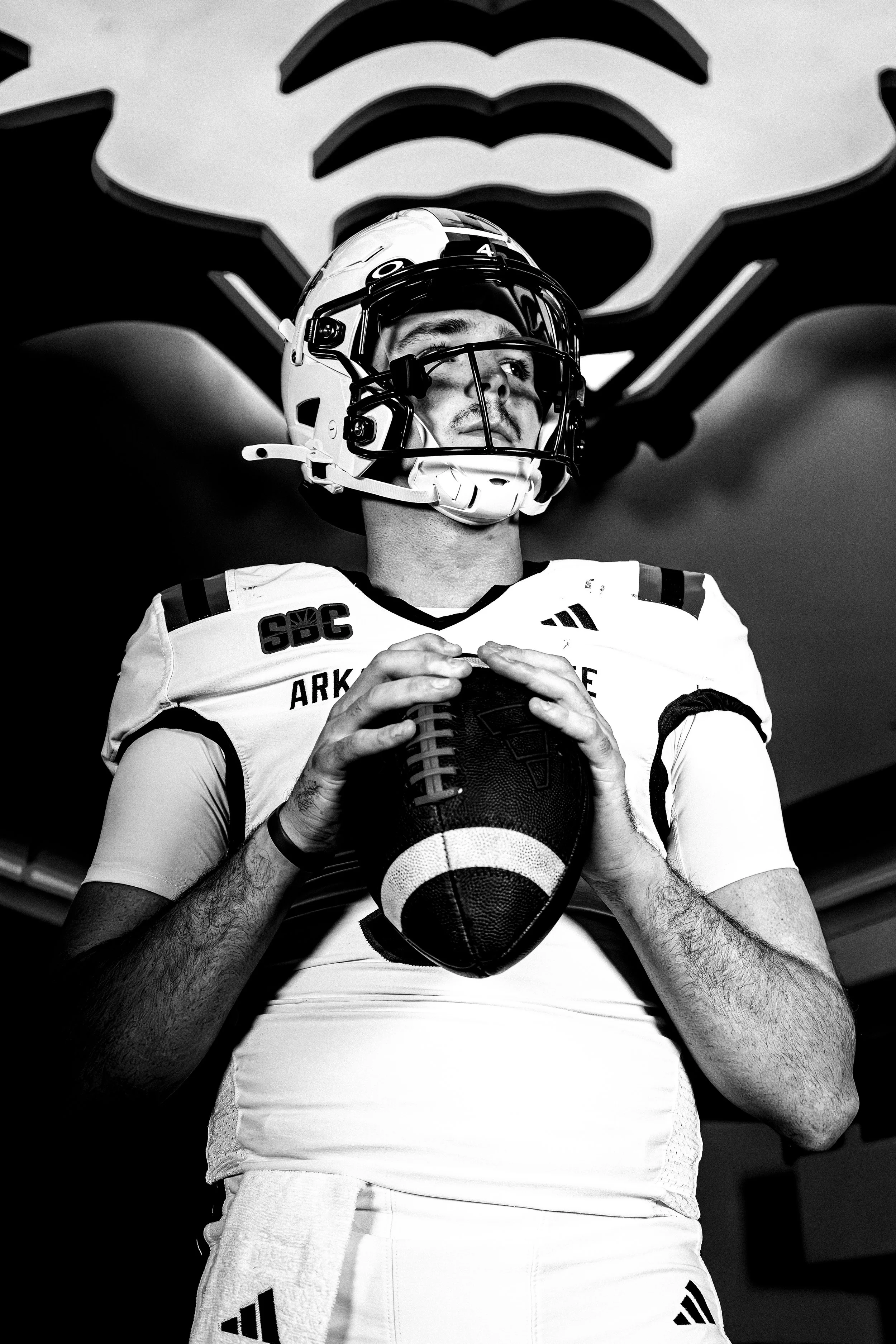 Trey in Arkansas State uniform holding a football, wearing a helmet and visor.