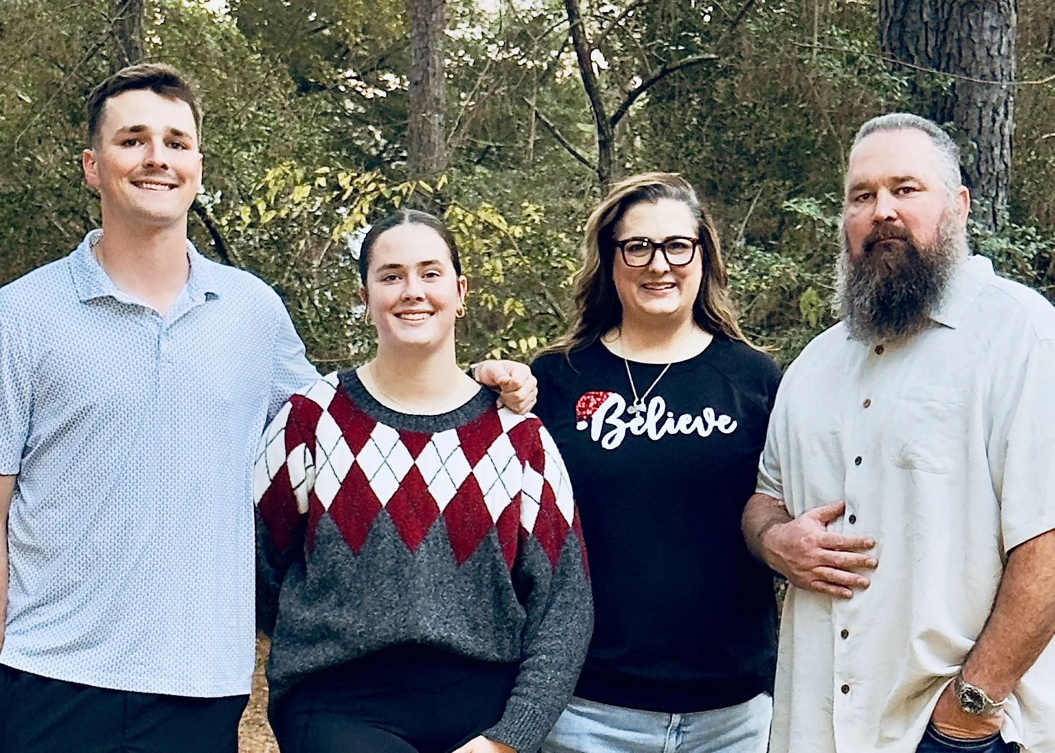 The Owens family standing outdoors in a wooded area, smiling at the camera.