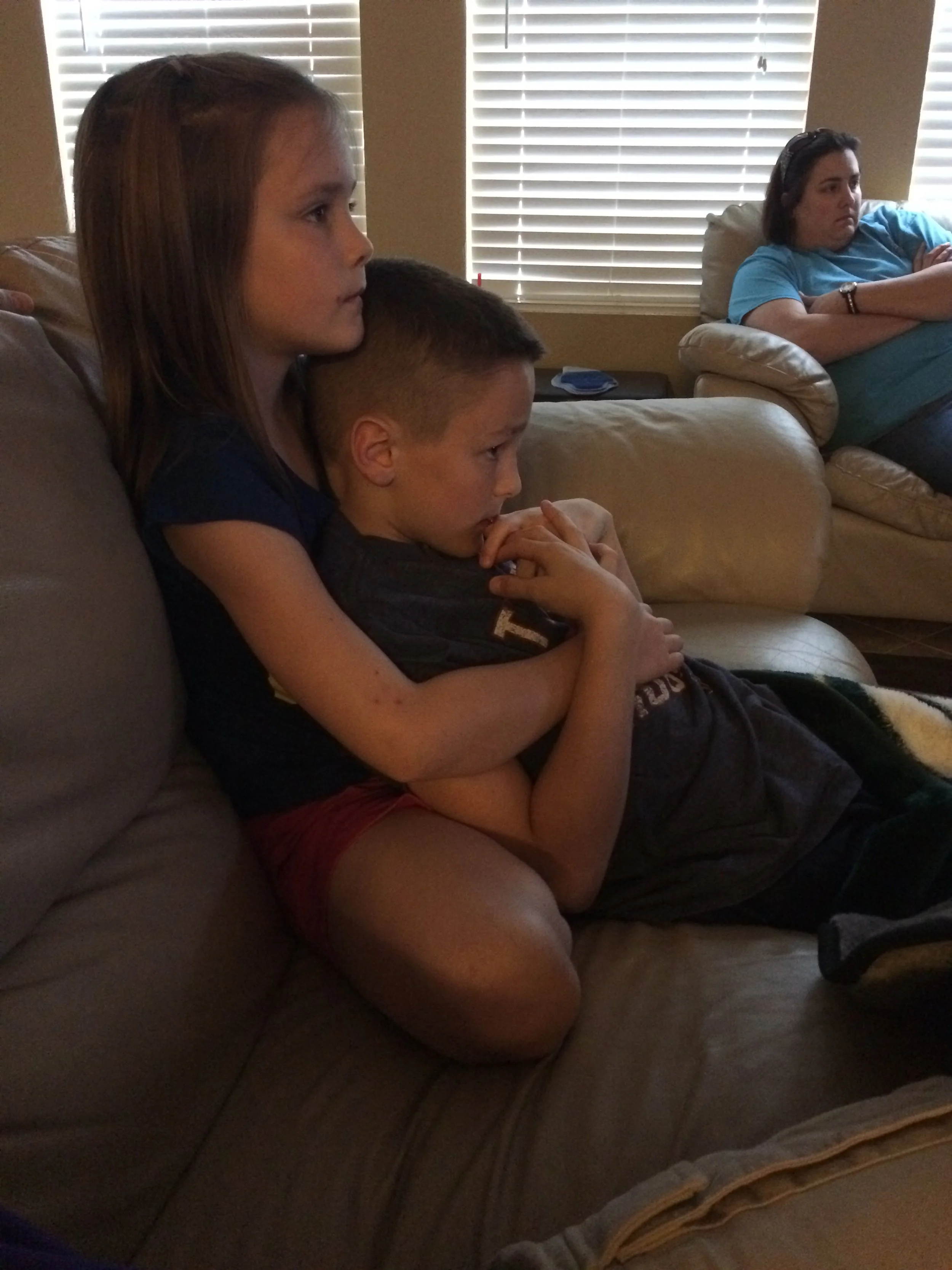 Trey and his sister sitting on a beige couch, watching a game intently.