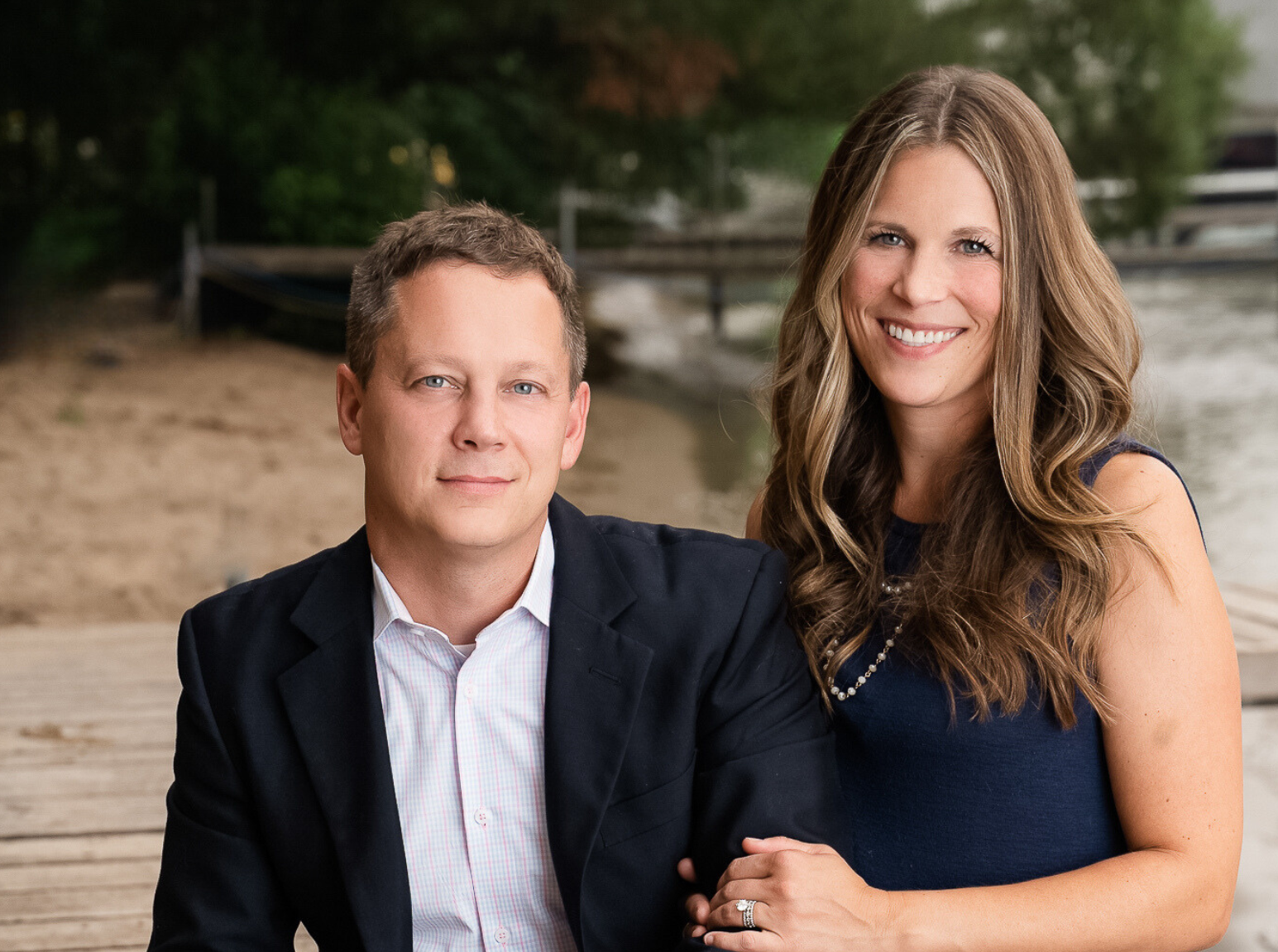 Andrew Beitler and Tiffany Beitler smiling in front of a beach at a lake