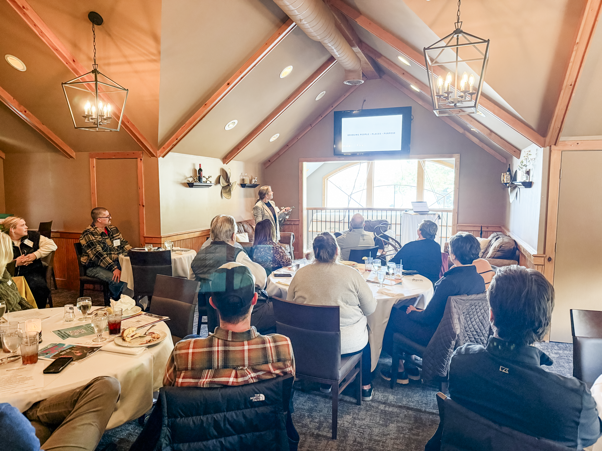 Tiffany Beitler presenting to a room of people with the words "Bridging people, places and purpose" on the screen