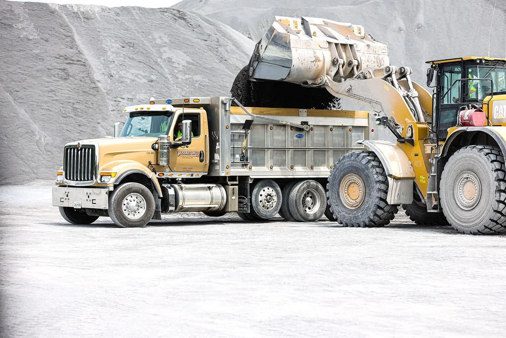 Creekstone dump truck and large yellow construction vehicle operating at an active quarry site, showcasing heavy equipment work, excavation, and material hauling services.