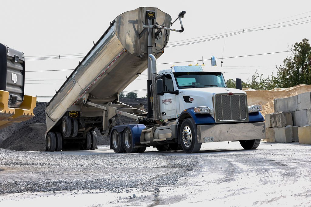 Creekstone dump truck with a raised bed unloading material at a construction site, with stacked concrete blocks and nearby construction equipment, highlighting heavy hauling and site-work operations.