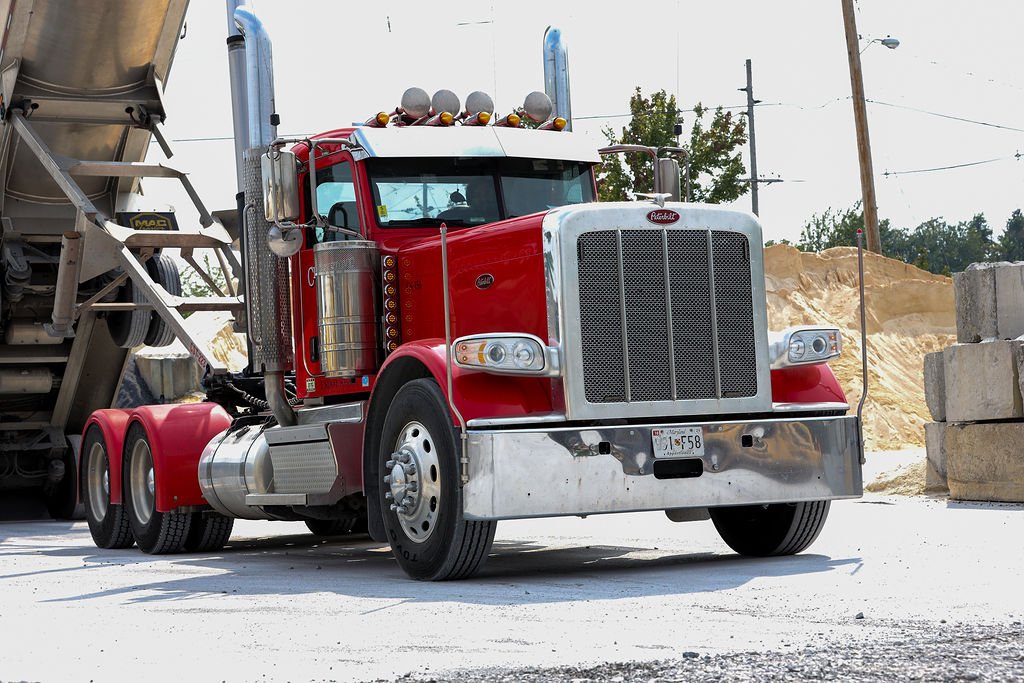 Creekstone red Peterbilt semi-truck parked on a construction site with sand piles and concrete blocks nearby, highlighting heavy hauling and construction site logistics.