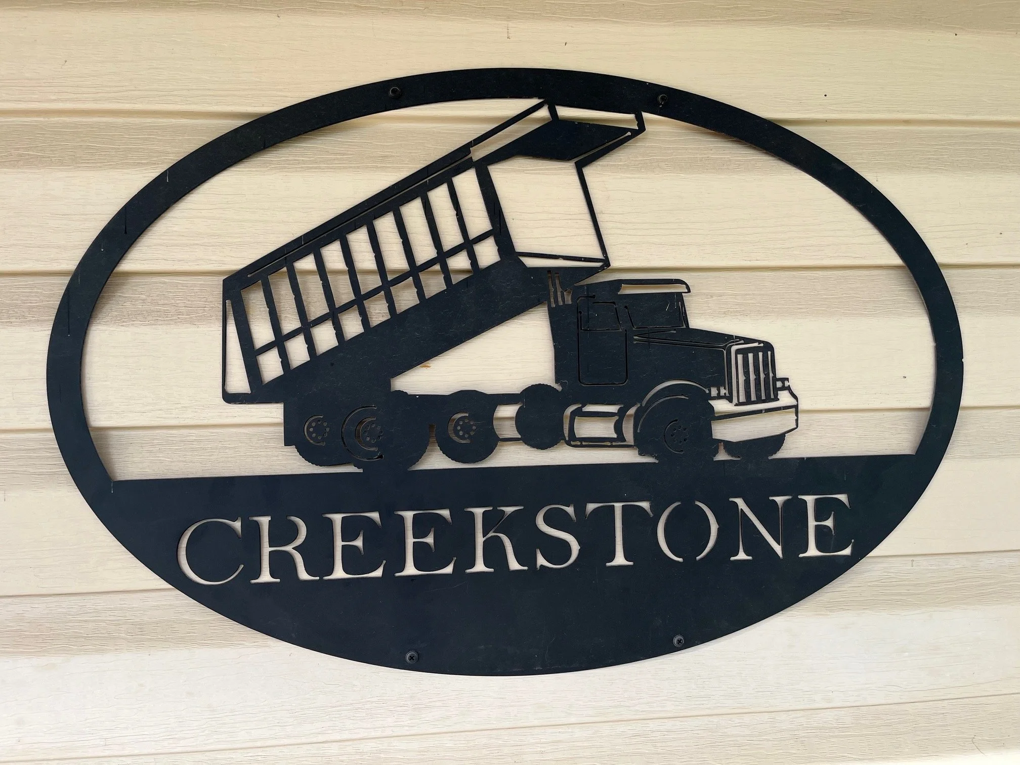 Metal sign with a dump truck graphic and the word 'CREEKSTONE' on a pale wooden wall.