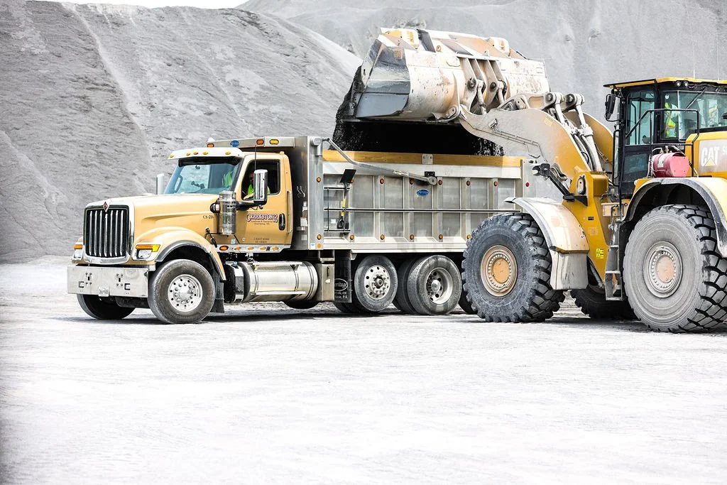 A large yellow dump truck and a yellow front loader working in a quarry or construction site.