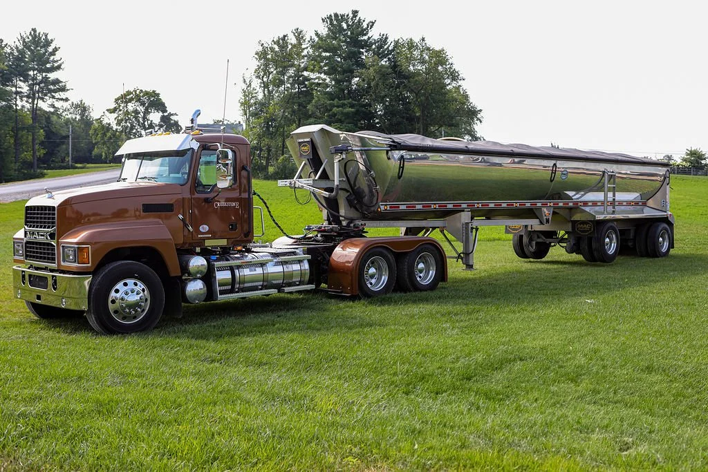 Close-up of Creekstone dump truck tires on the rear axle at a construction site, with a worker standing nearby, emphasizing heavy-duty trucking and site-work operations.