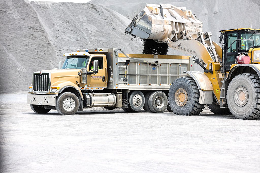 Creekstone dump truck and front loader operating in a sand and gravel quarry, showcasing aggregate extraction and heavy equipment operations.