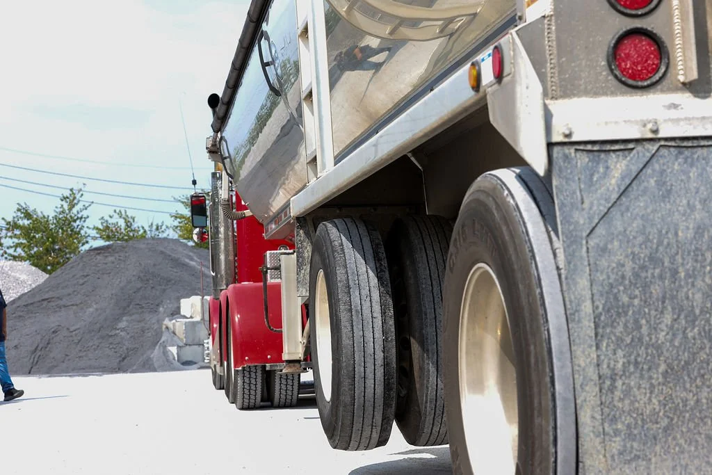 Creekstone semi-truck with a tanker trailer parked at a quarry-style construction site with a dirt hill and construction equipment in the background, highlighting heavy hauling and tanker transport services.