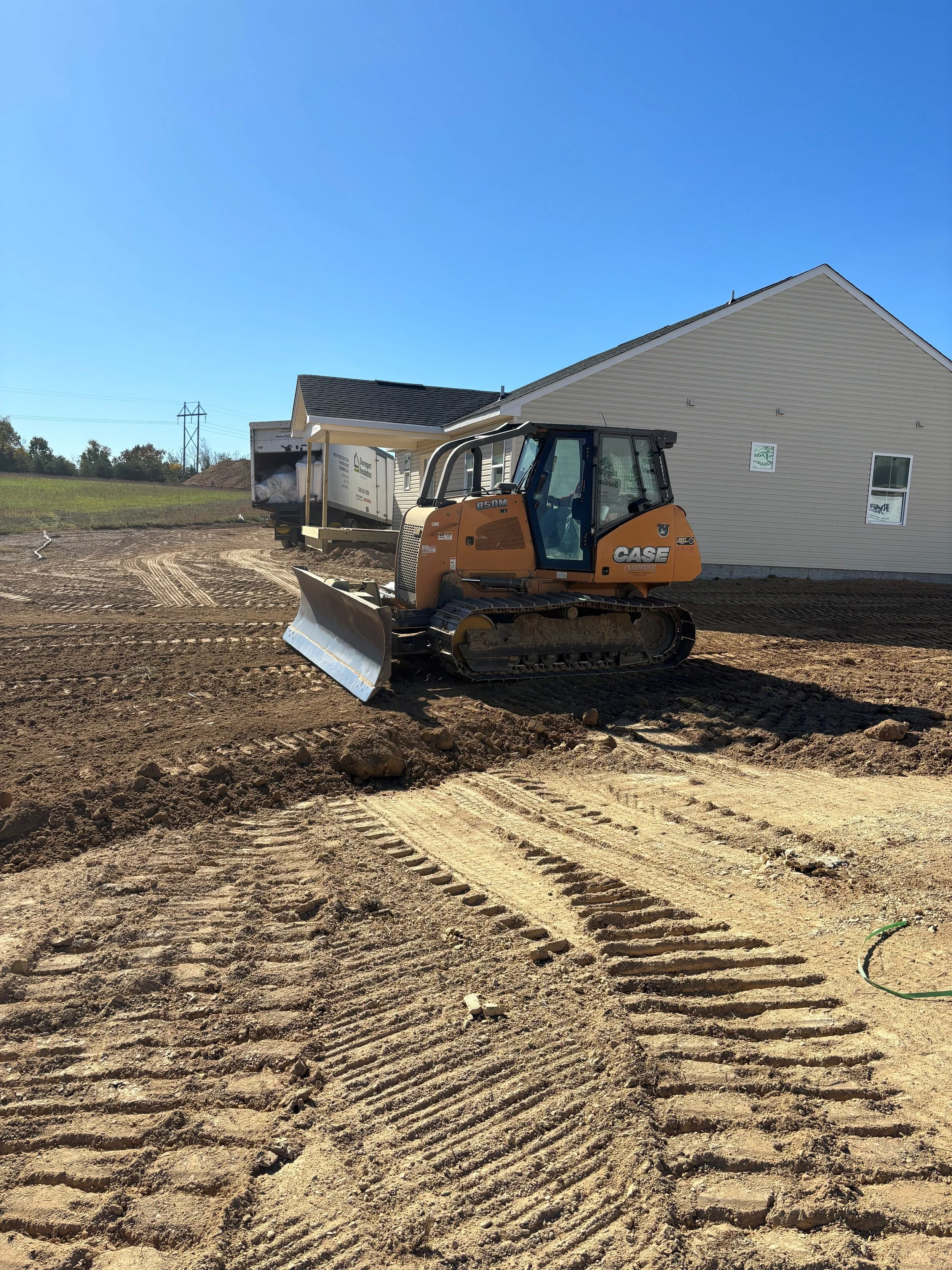 Creekstone small orange bulldozer pushing dirt at a construction site near a house under construction on a clear day, highlighting grading and site-preparation services.